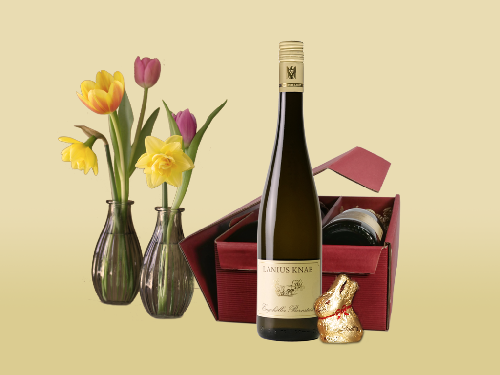 Geschenkkarton mit Weinflasche und Schokoladen-Osterhase, im Hintergrund Frühlingsblumen